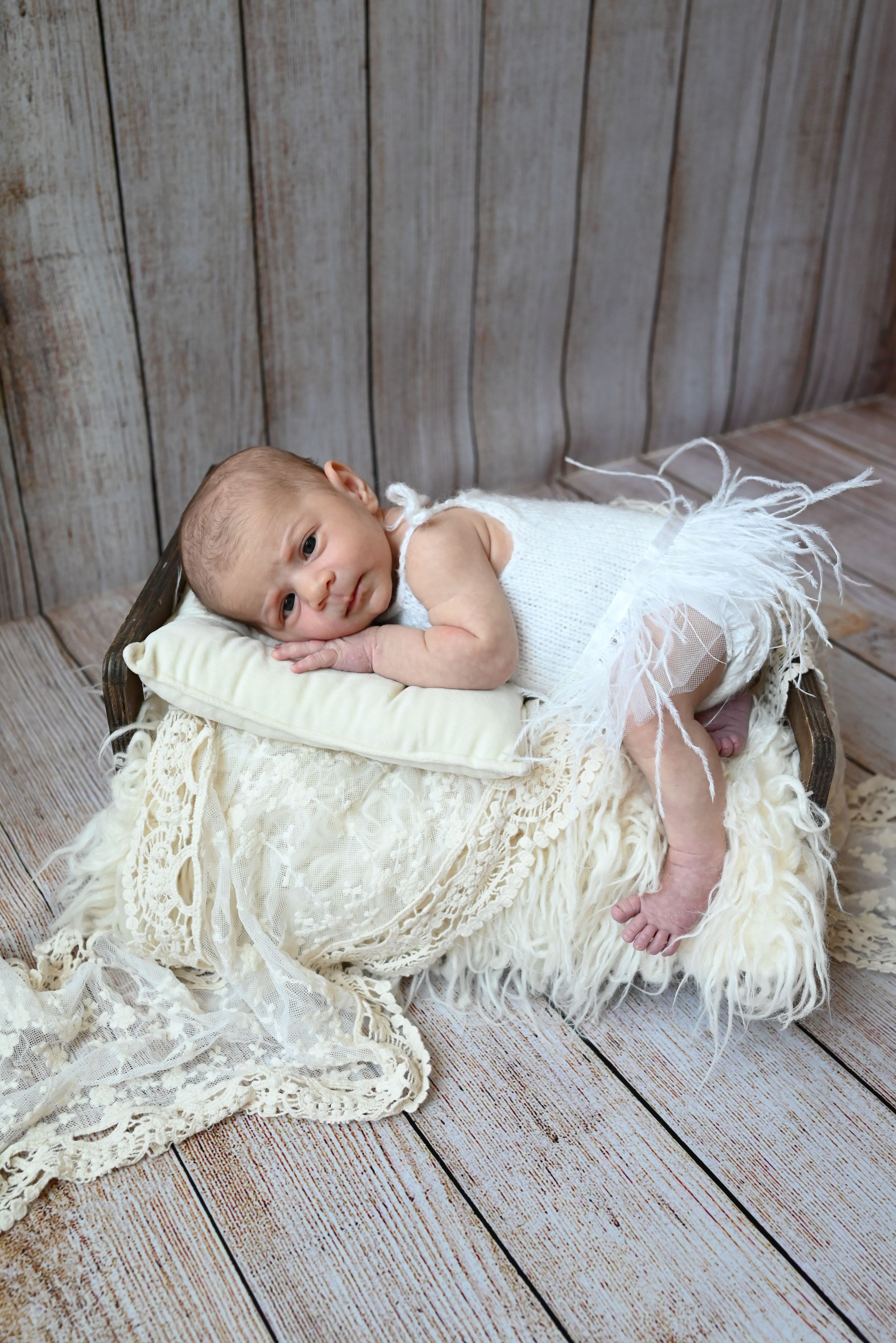 A small baby wrapped in delicate cream lace fabric lies on rustic wooden floor boards in a sequence of similar poses.