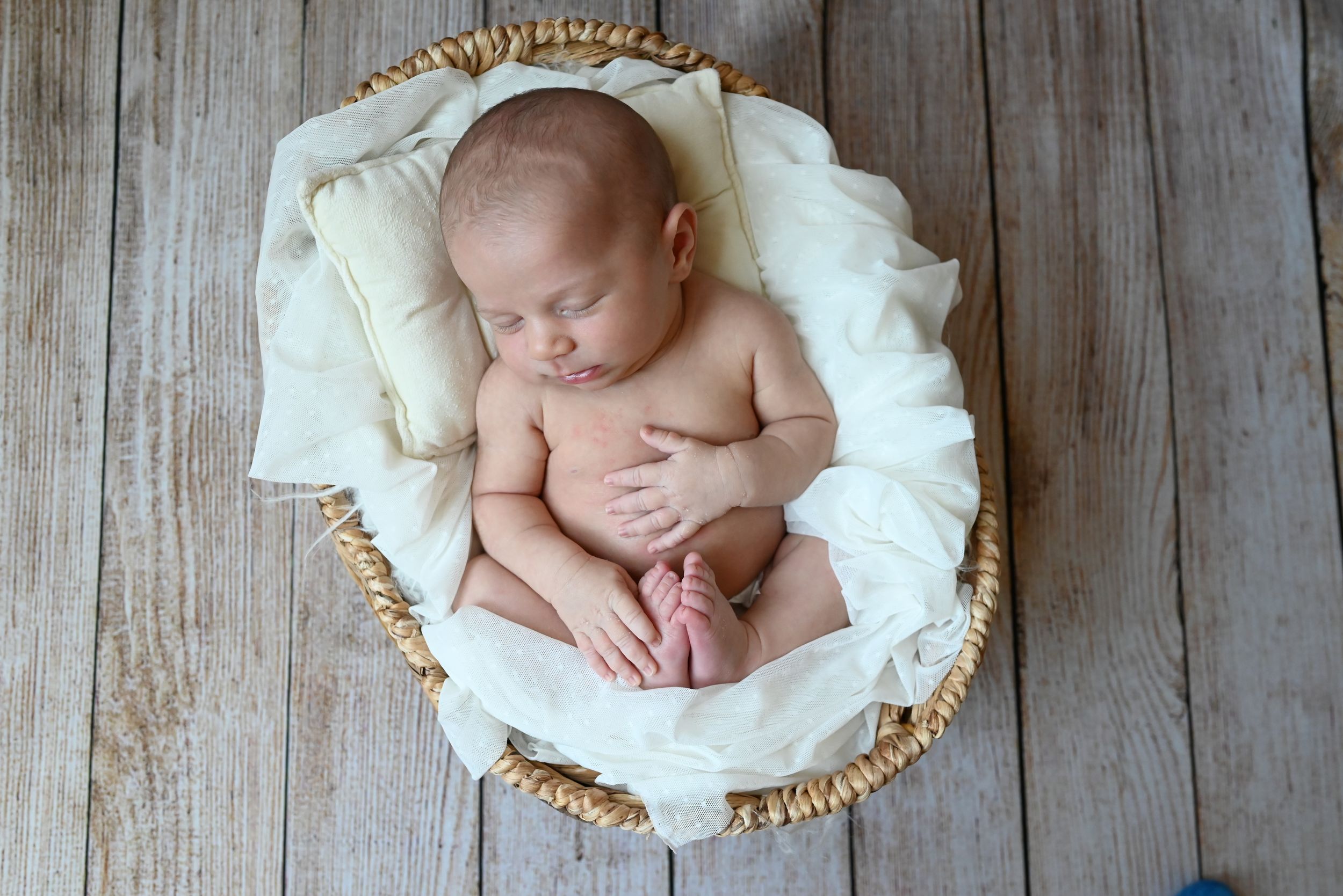 Newborn baby sleeping peacefully in woven basket lined with soft white fabric on wooden floor.
