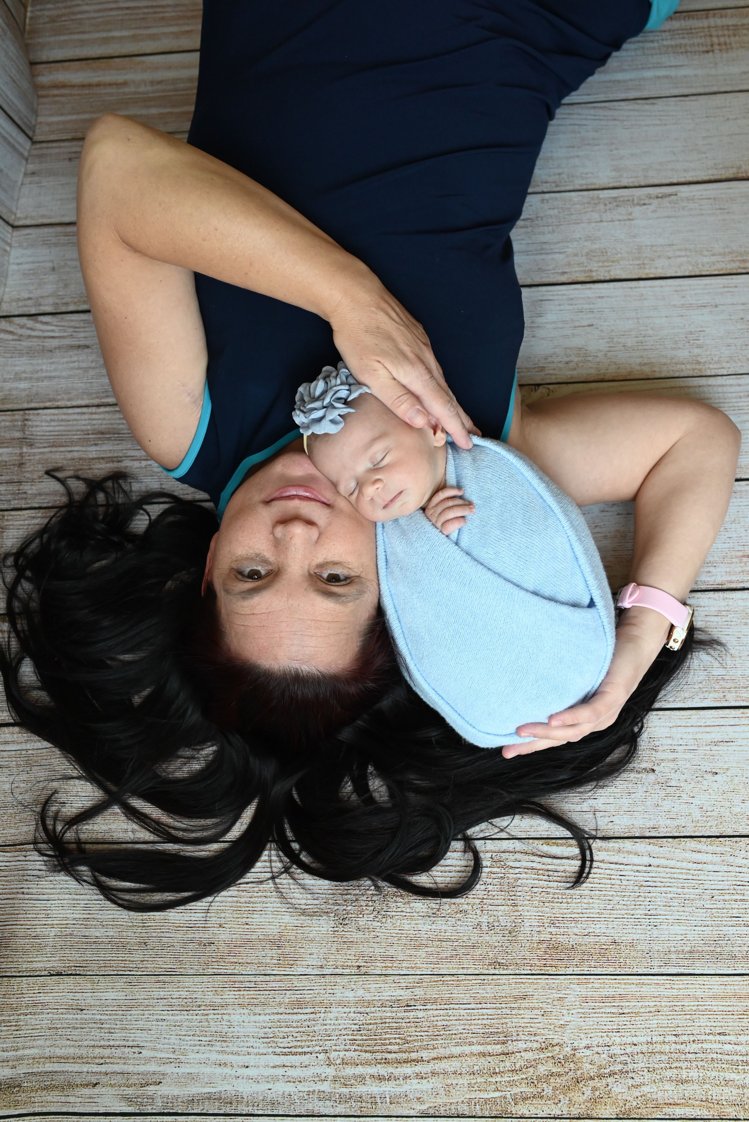 Person in dark top lying on wooden floor with light-colored face mask covering their face.