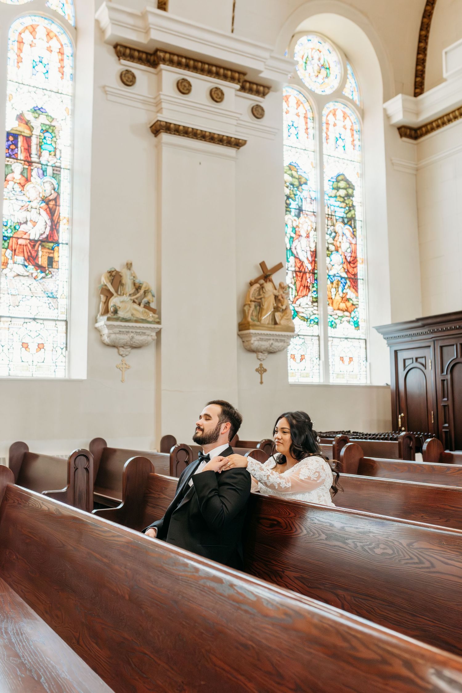 A person sits in a wooden church pew gazing upward at stained glass windows in an ornate historic chapel interior.