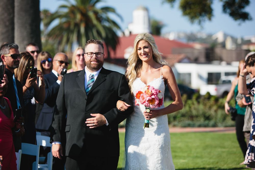 Wedding party celebrates outdoors with white and pink floral bouquets on a sunny day.