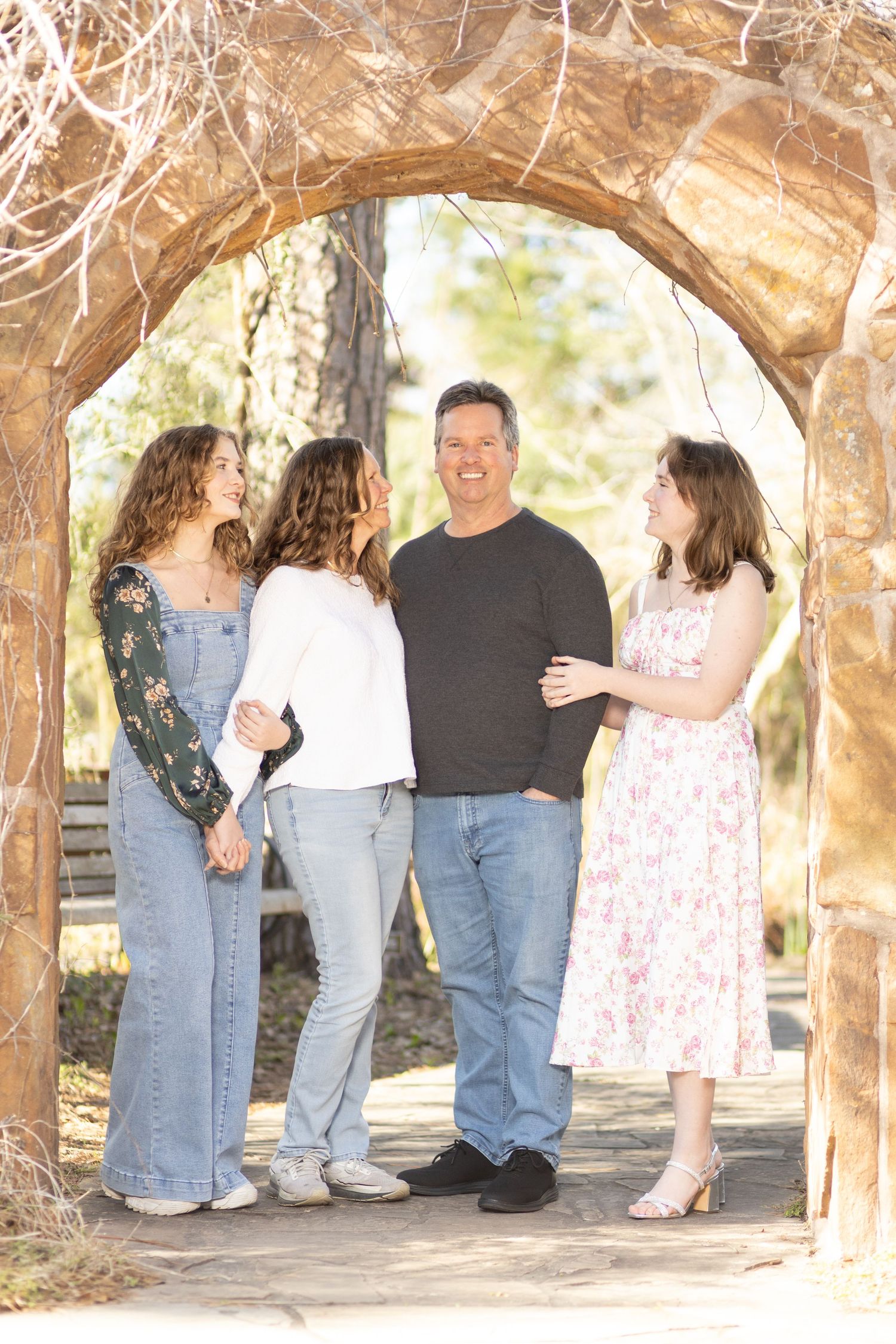 A group stands together under a stone archway in a casual outdoor setting on a sunny day.