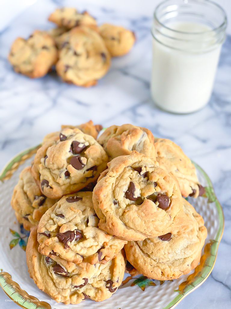 Homemade chocolate chip cookies arranged on a decorative plate with a glass of milk.