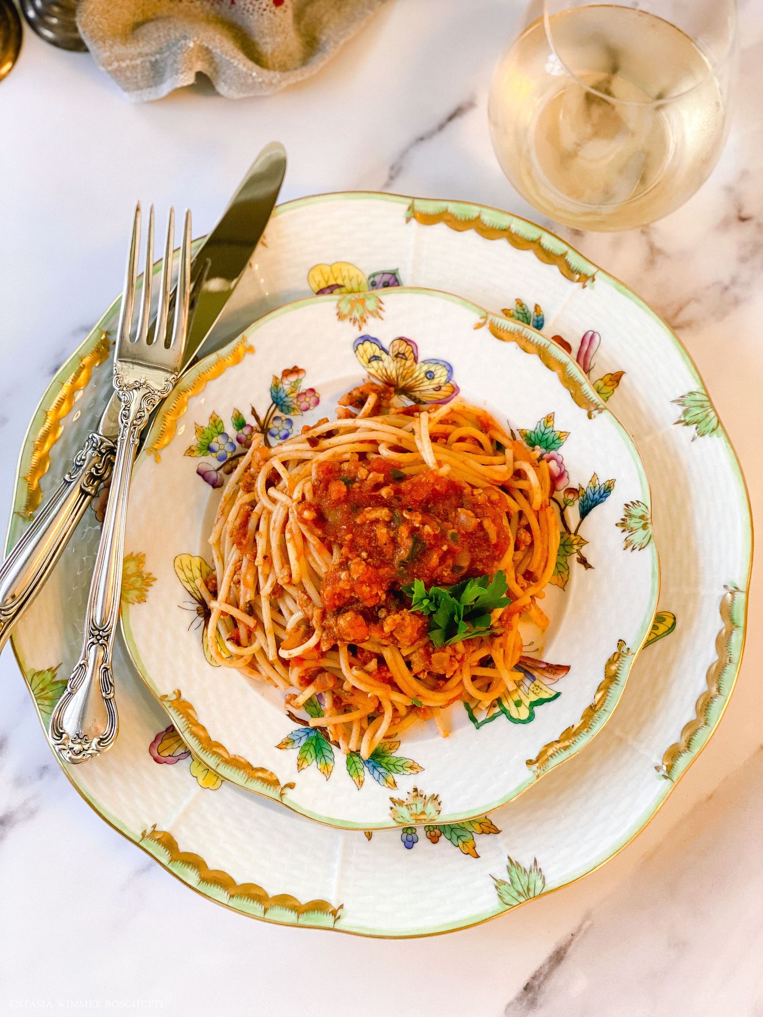 Spaghetti with meat sauce garnished with parsley served on floral-patterned plates.