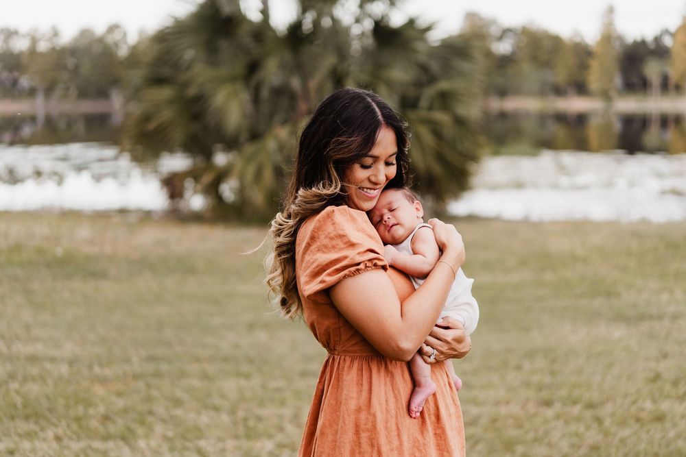 A tender moment captured outdoors as a woman in a peach dress embraces a crying baby in a grassy field.