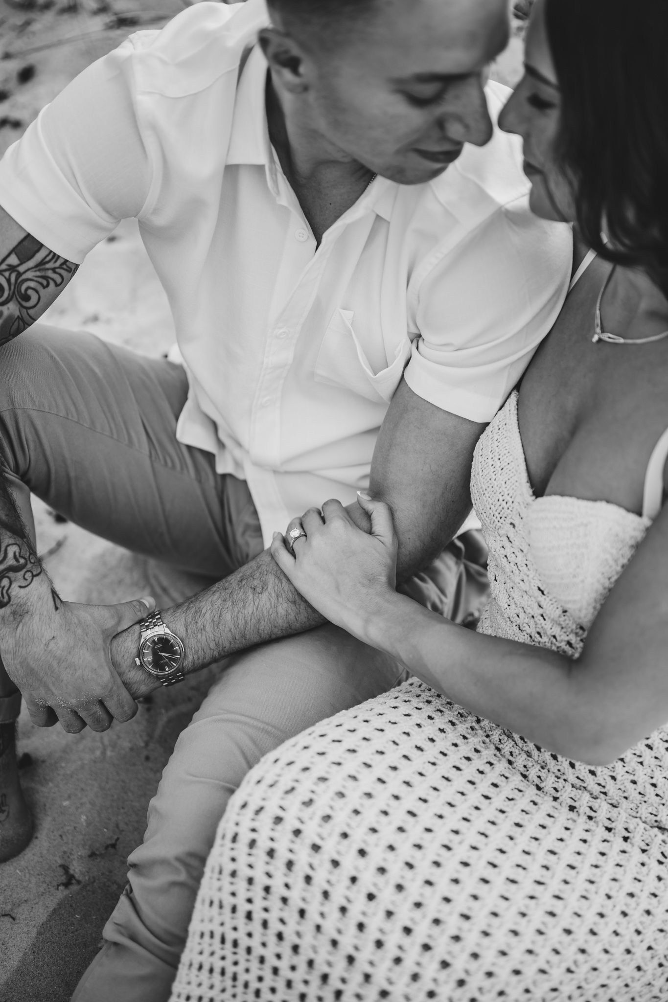 Black and white intimate photo of couple sitting close together on beach.