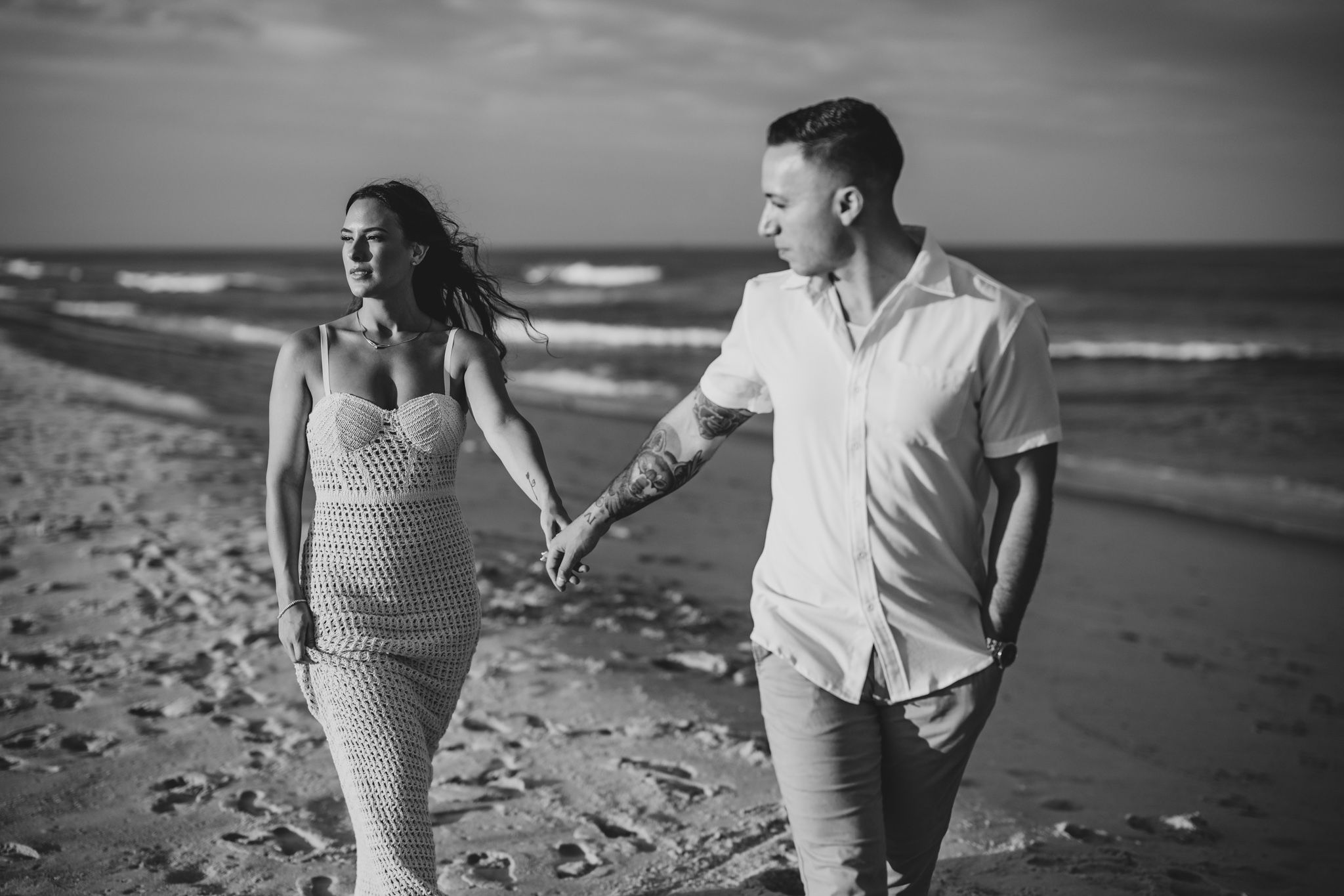Black and white beach photoshoot with couple walking along shoreline.