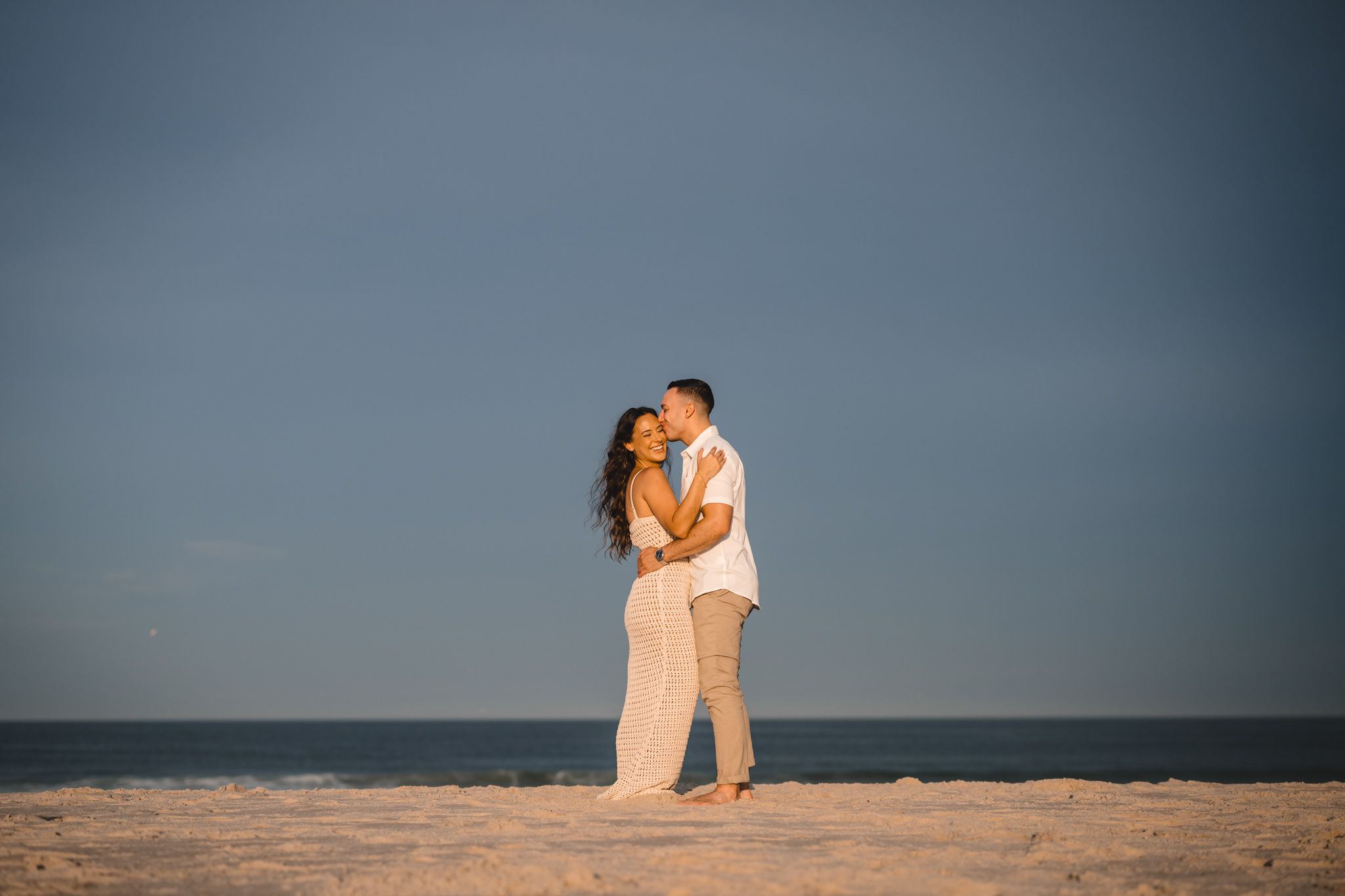 Silhouetted figures embrace on beach against dramatic blue sky.