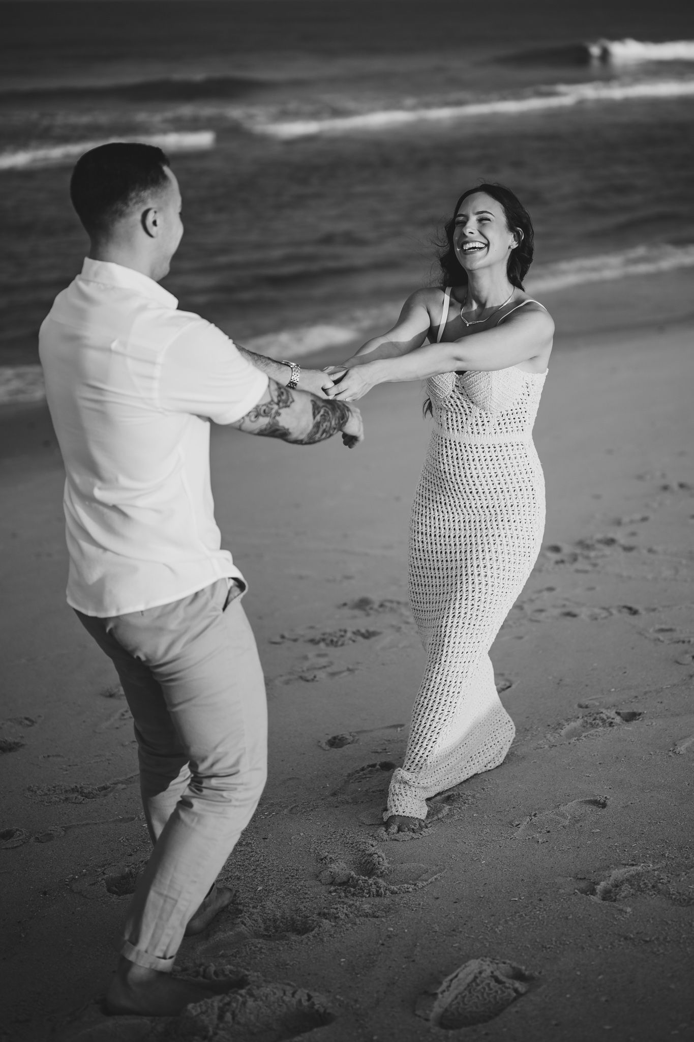 Black and white photo of couple dancing and spinning on beach.
