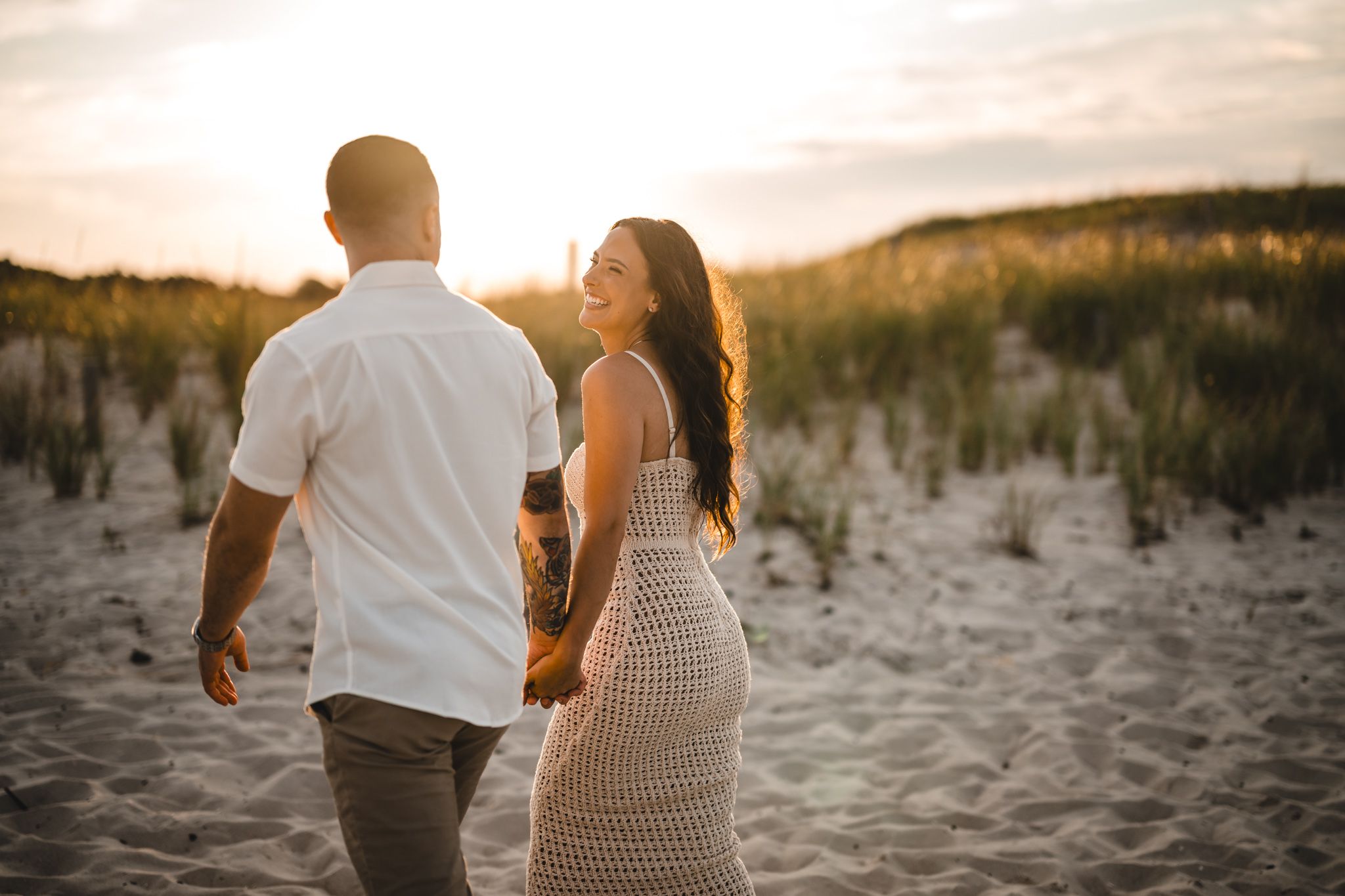 Silhouetted couple dancing on beach with sun setting behind dunes.