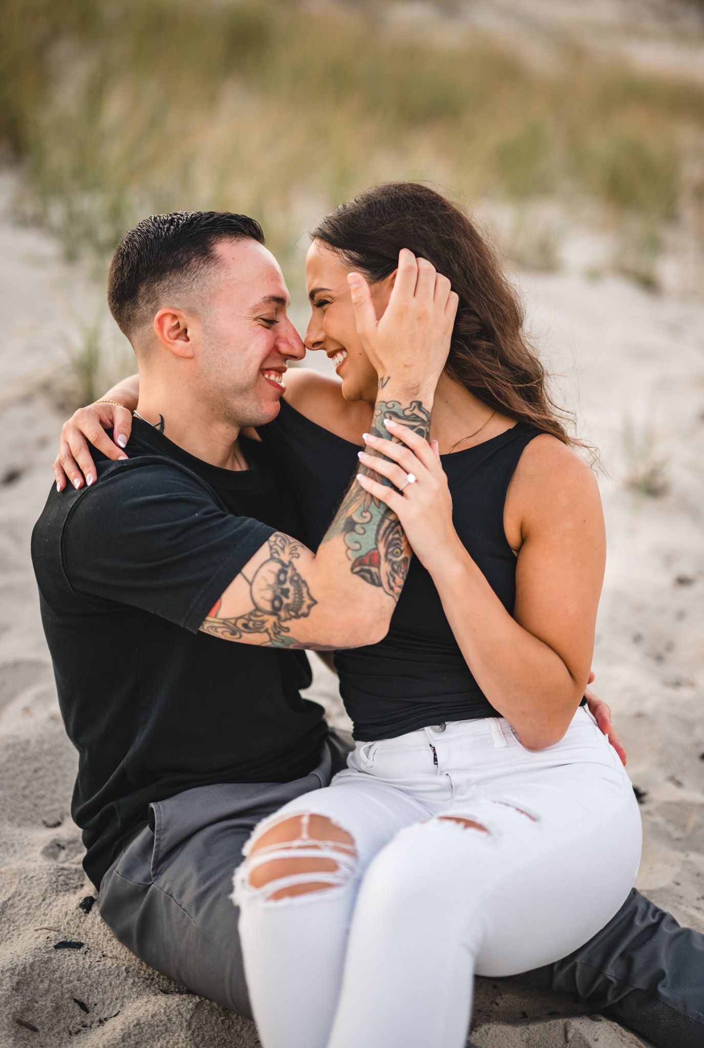Intimate beach portrait of couple sitting close together on sand.