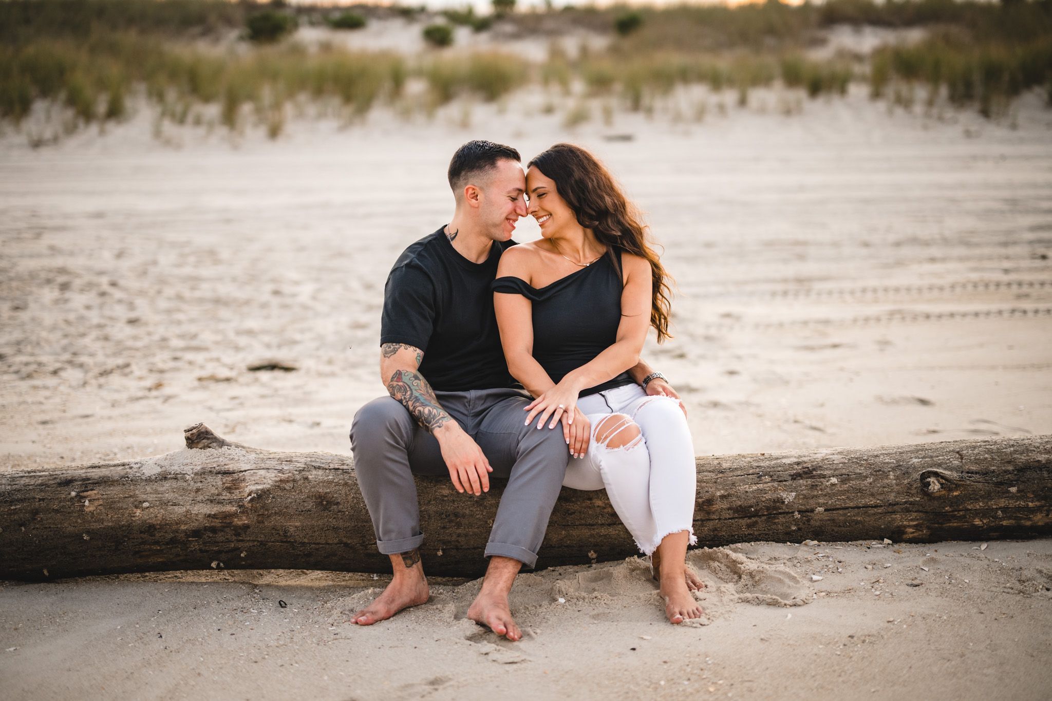 Couple sharing tender moment while seated on driftwood at beach.