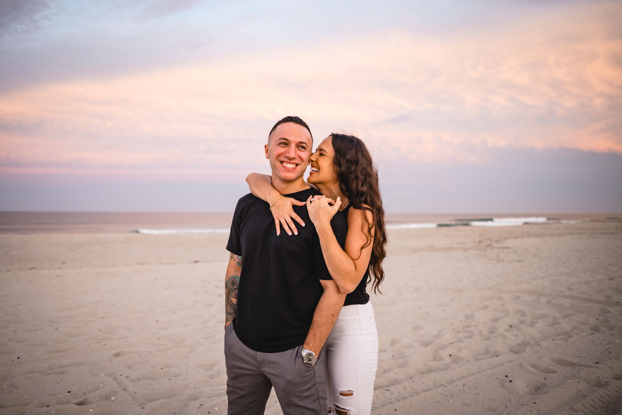 Beach engagement session with couple embracing during sunset.