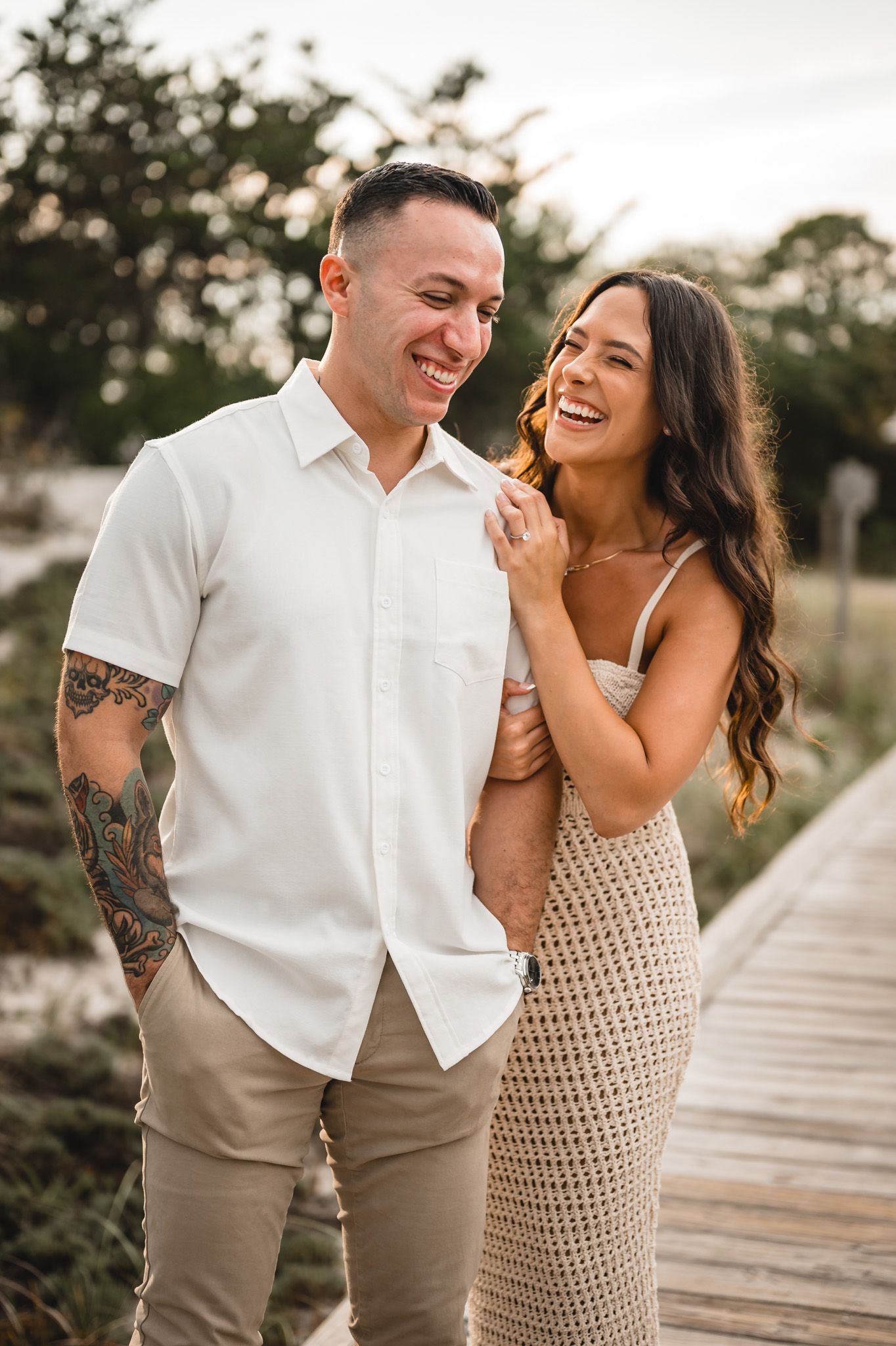 A couple shares joyful laughs together on a wooden boardwalk near the beach.