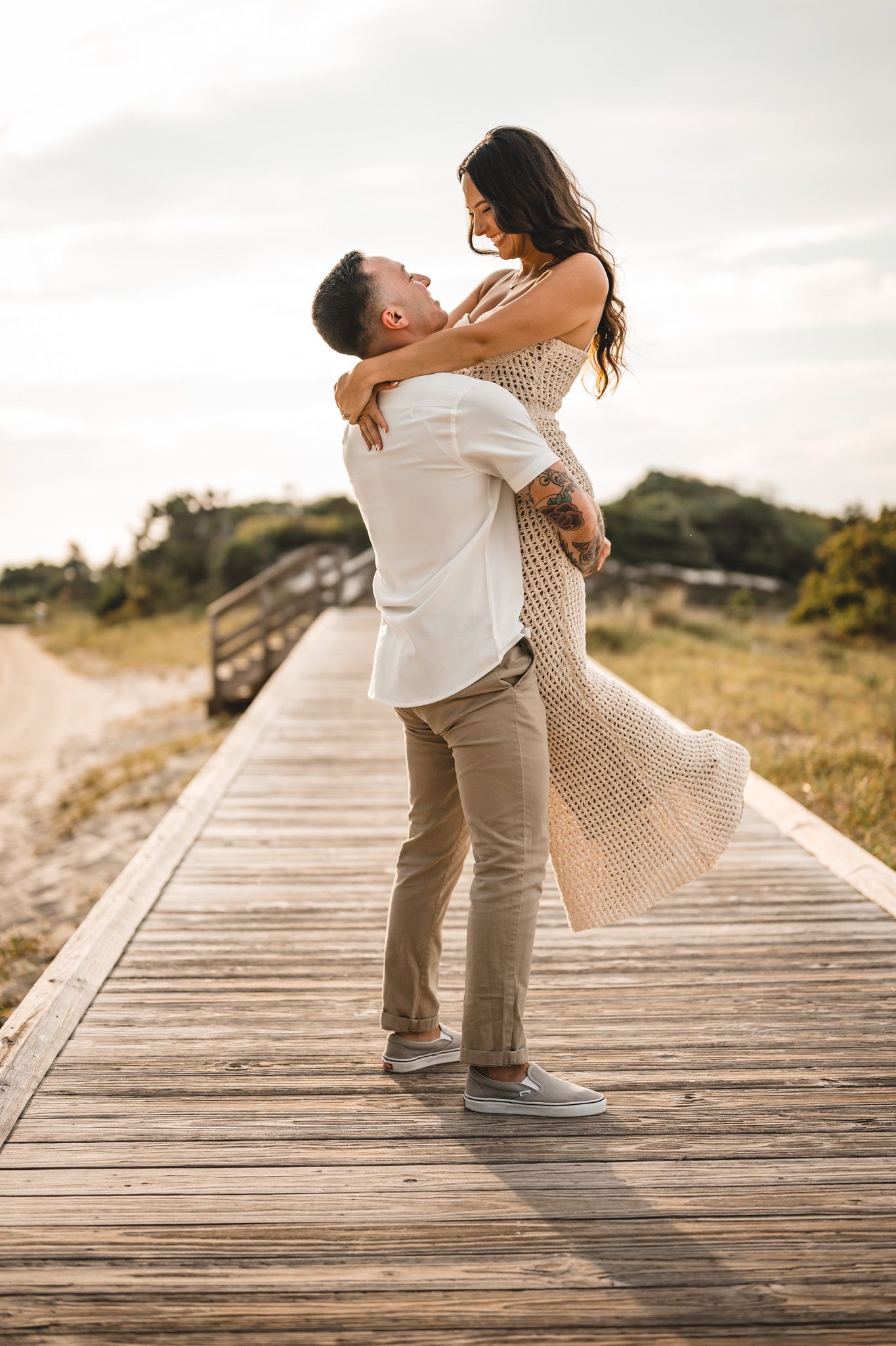 A couple dances and embraces on a wooden boardwalk by the beach.