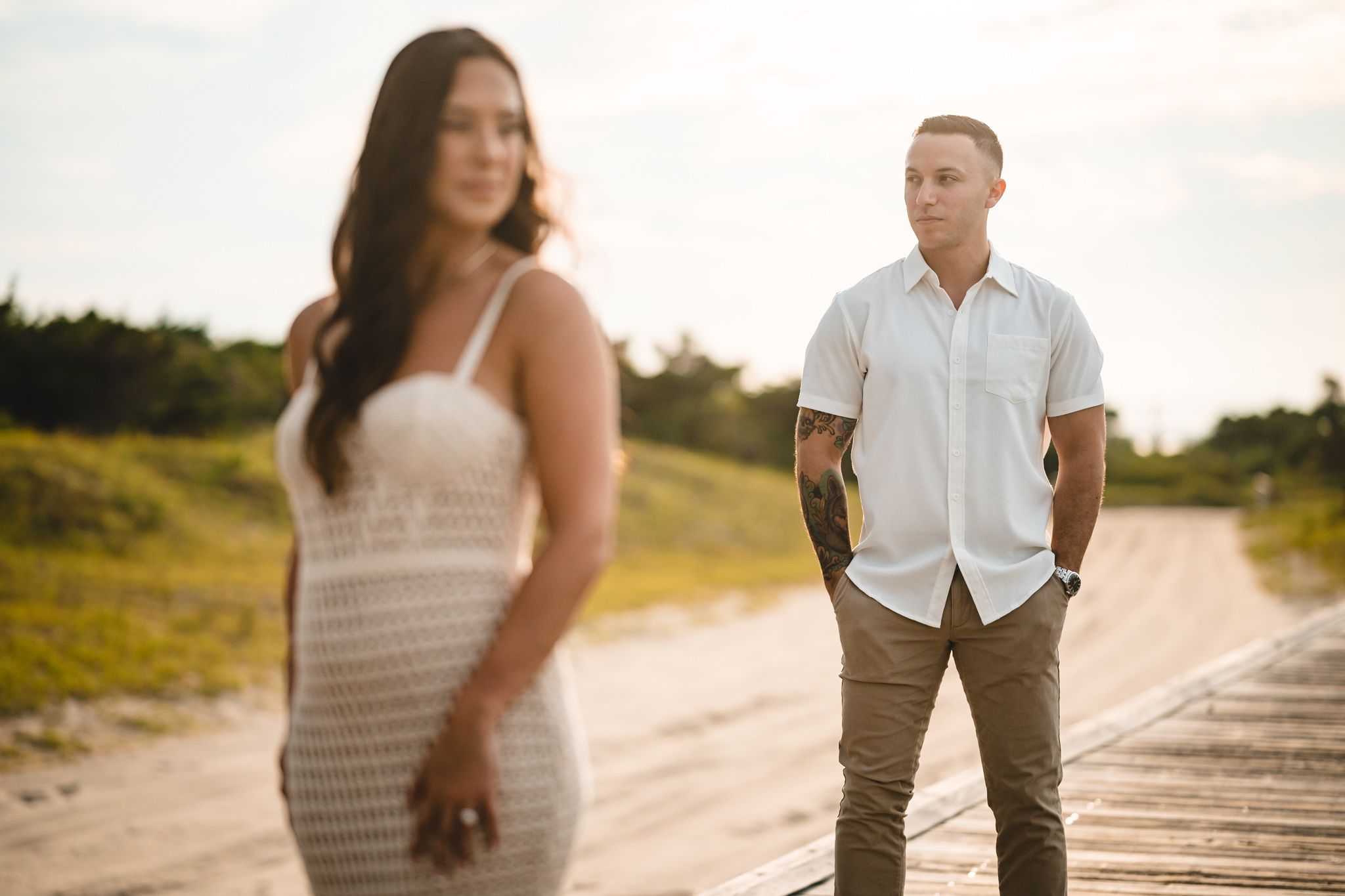 Two people strolling on a sandy path at sunset with natural vegetation in background.