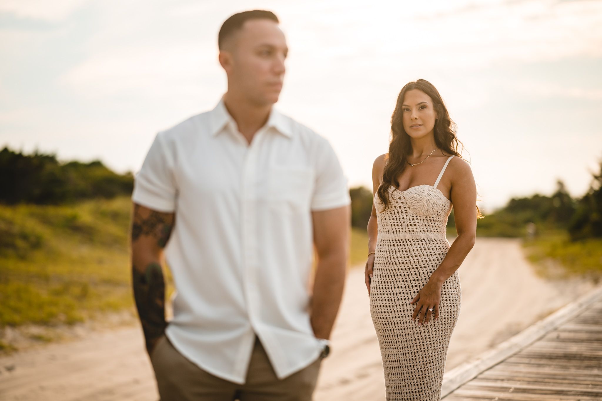 Couple in casual beach attire walking along a sandy path during golden hour.