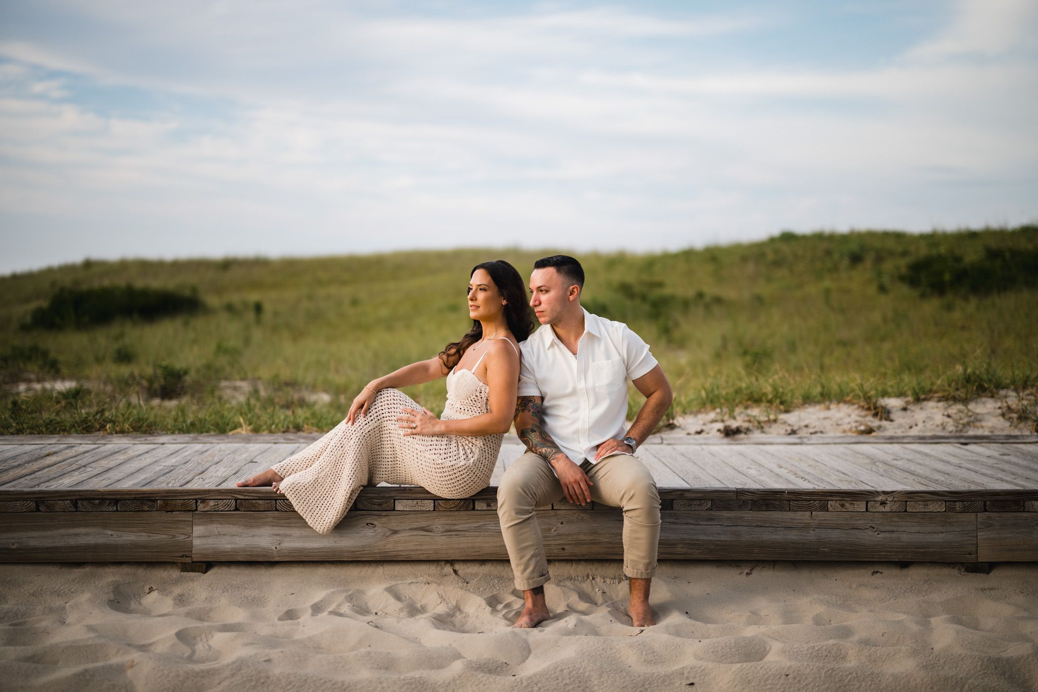 Romantic beach photoshoot with couple sitting on wooden boardwalk at sunset.