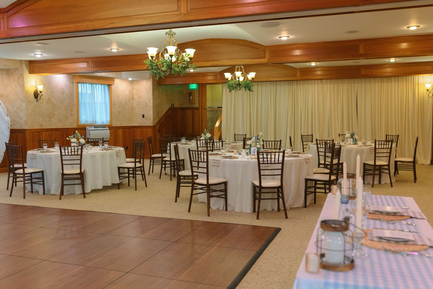 Elegant banquet hall with round white tables, dark wooden chairs, chandeliers and warm lighting creates an inviting atmosphere.