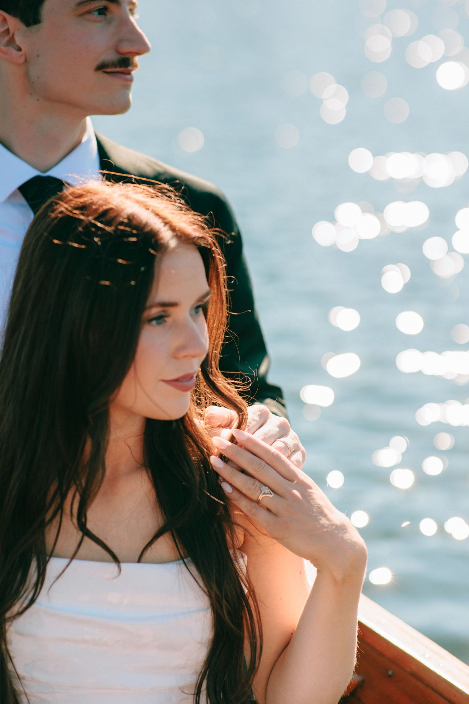A romantic couple poses on a boat with sparkling sunlight reflecting on the water behind them.