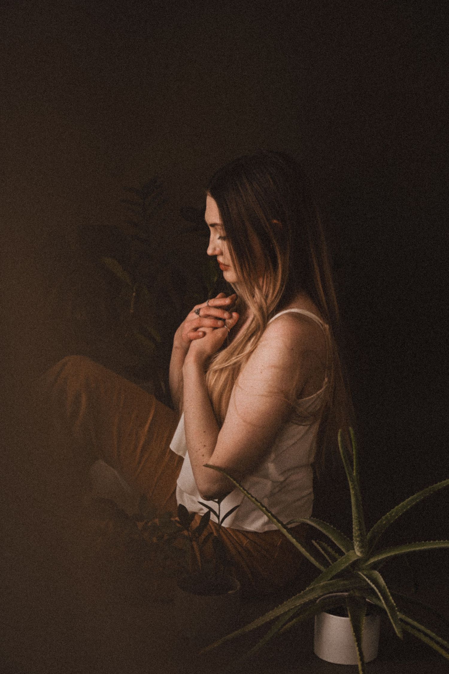 Moody boudoir photoshoot with soft lighting and indoor plants creating intimate atmosphere.