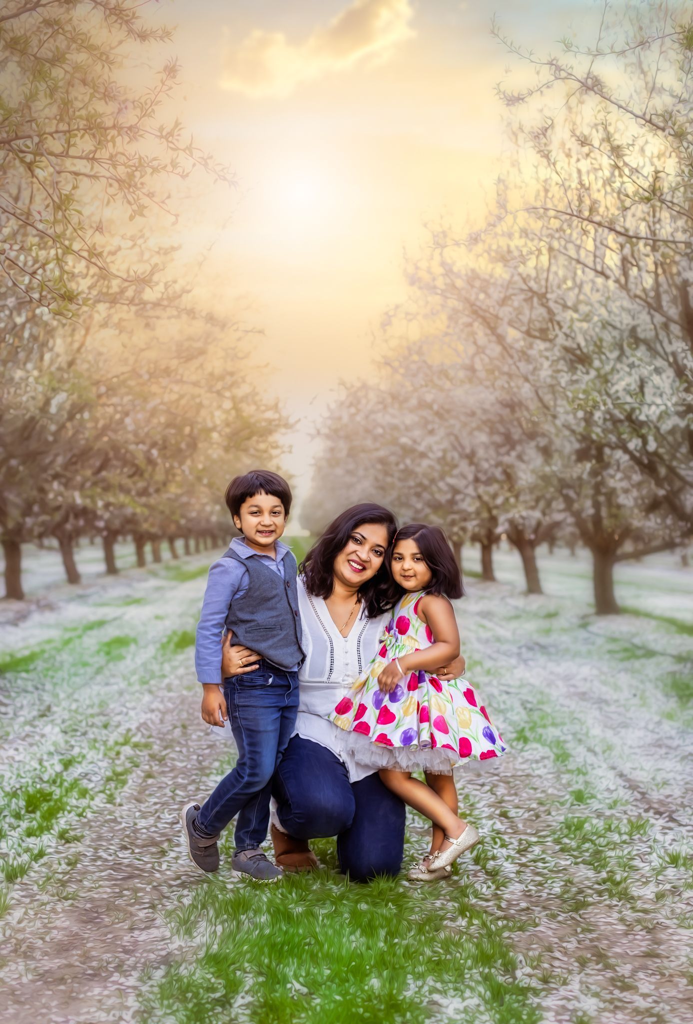 Family candid photoshoot at sunset in a dreamy almond orchard with white blossoms and warm golden light.