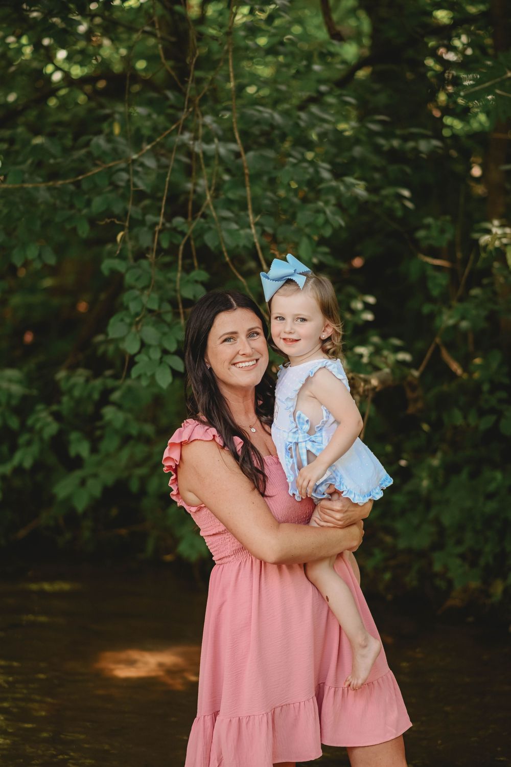 A sweet moment captured in matching pink dresses against a leafy green background.