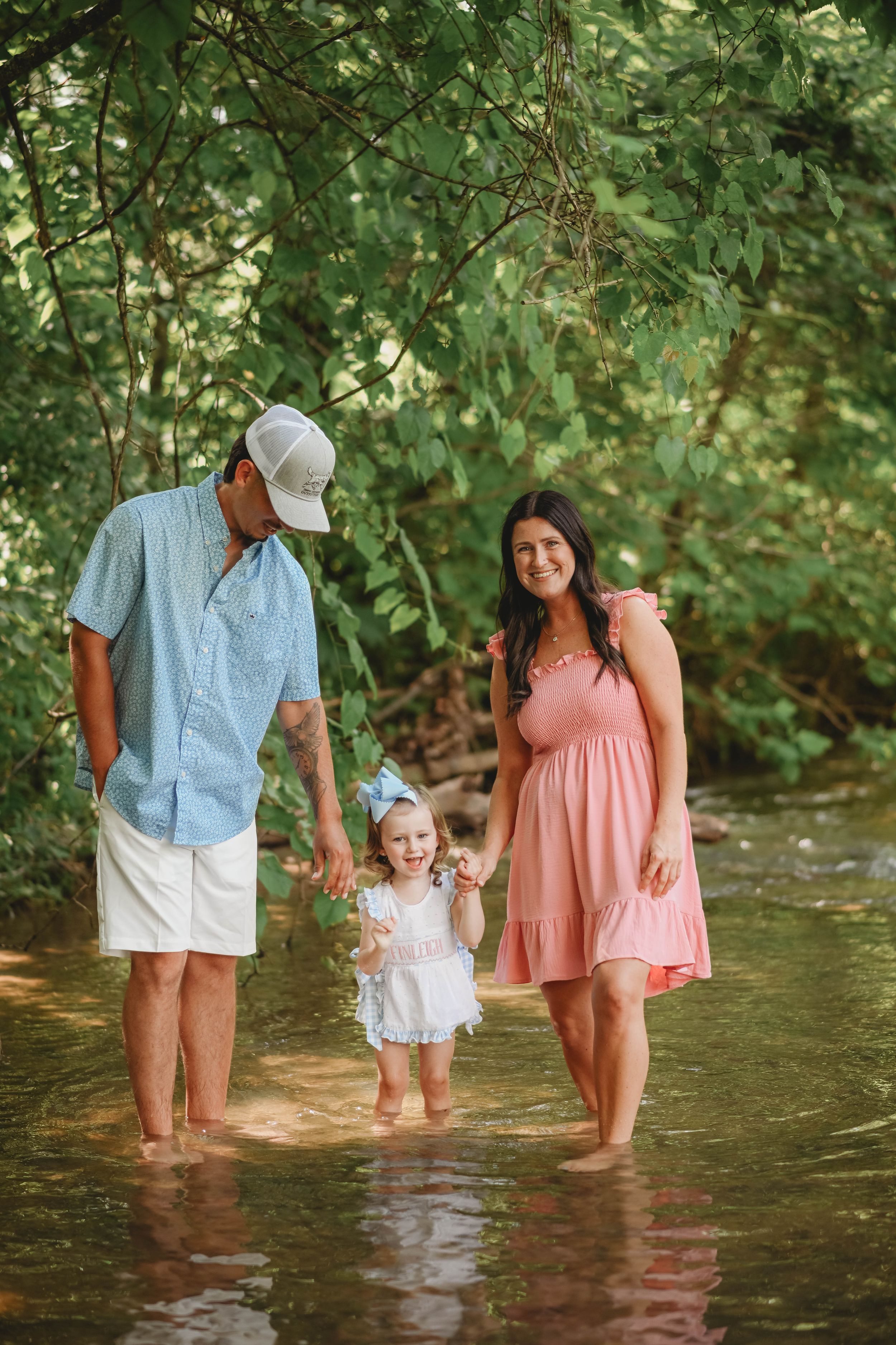 A family wades together through shallow creek water on a sunny summer day.