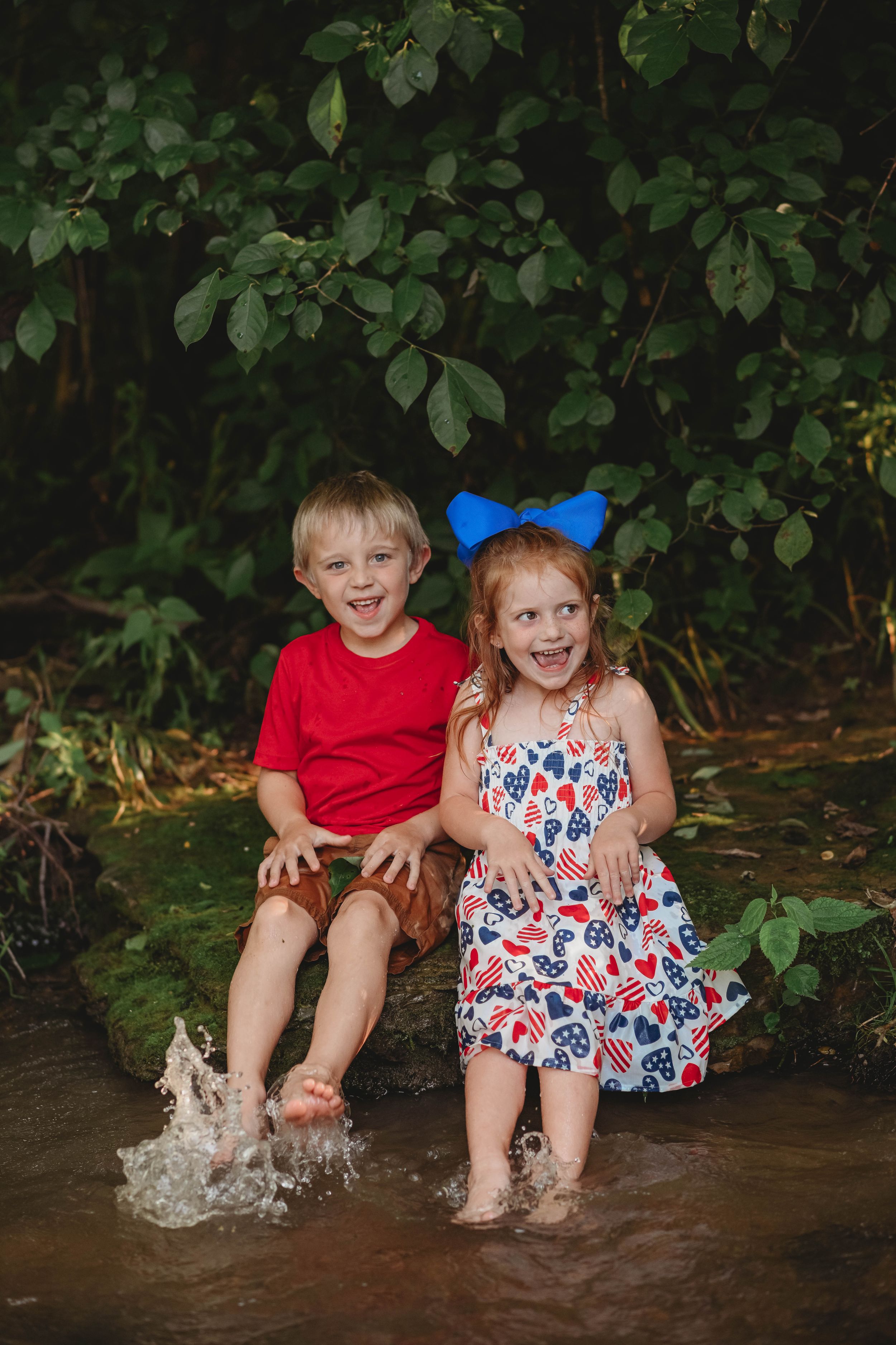 Children sit at the edge of a creek splashing their feet in the water.