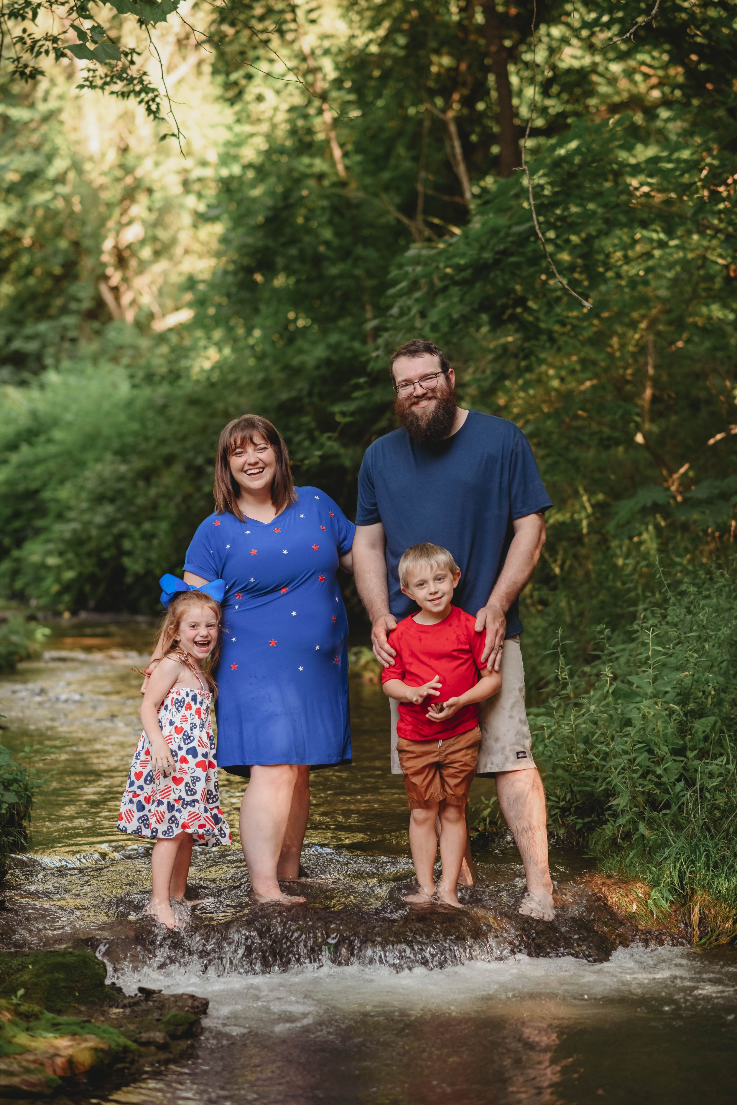 Family members create joyful splashes while standing in a shallow stream surrounded by greenery.