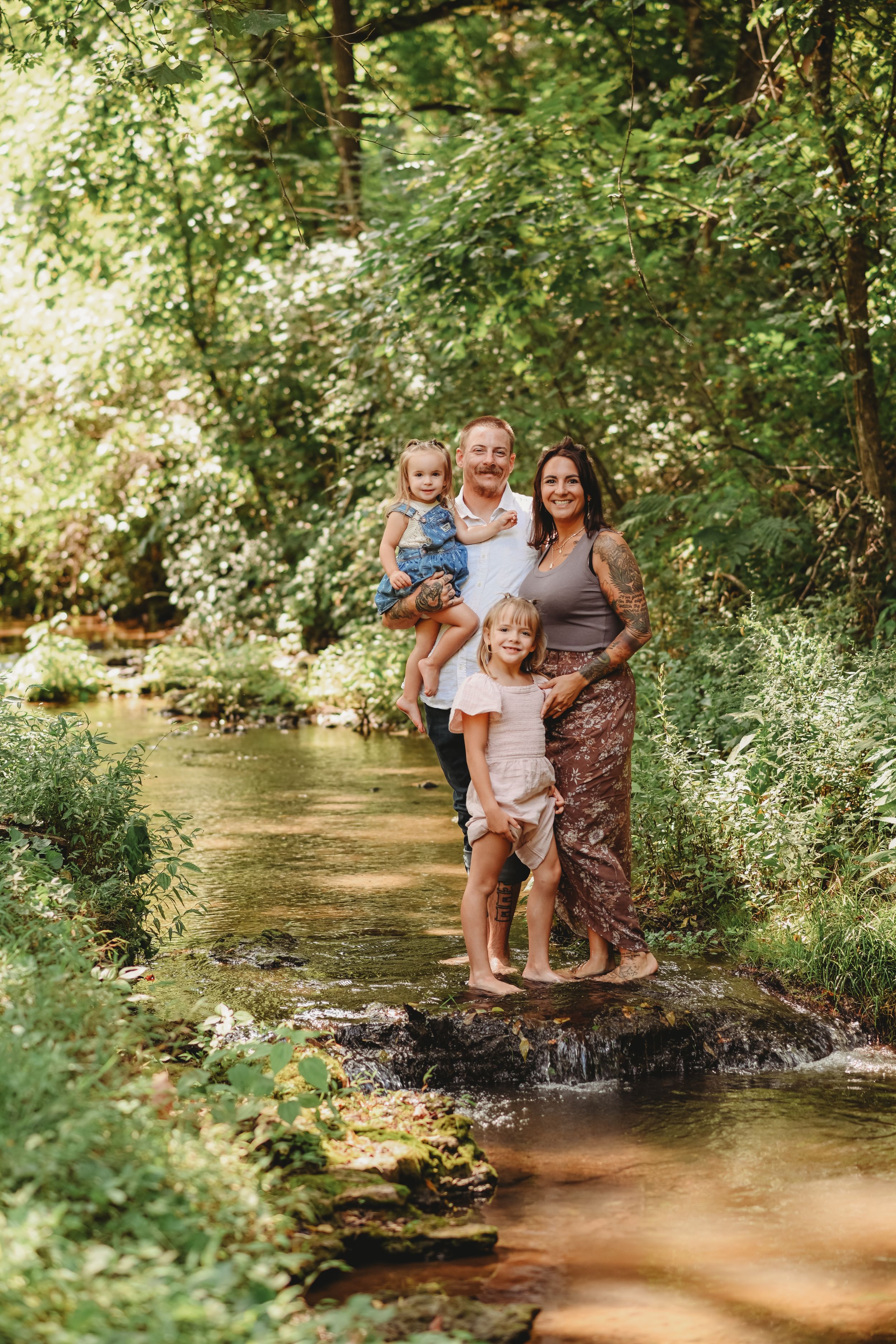 Family enjoying time together on rocks by a peaceful woodland stream.