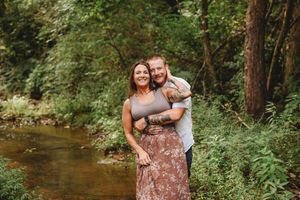 A couple shares an intimate moment in a lush green forest setting during a summer photo session.