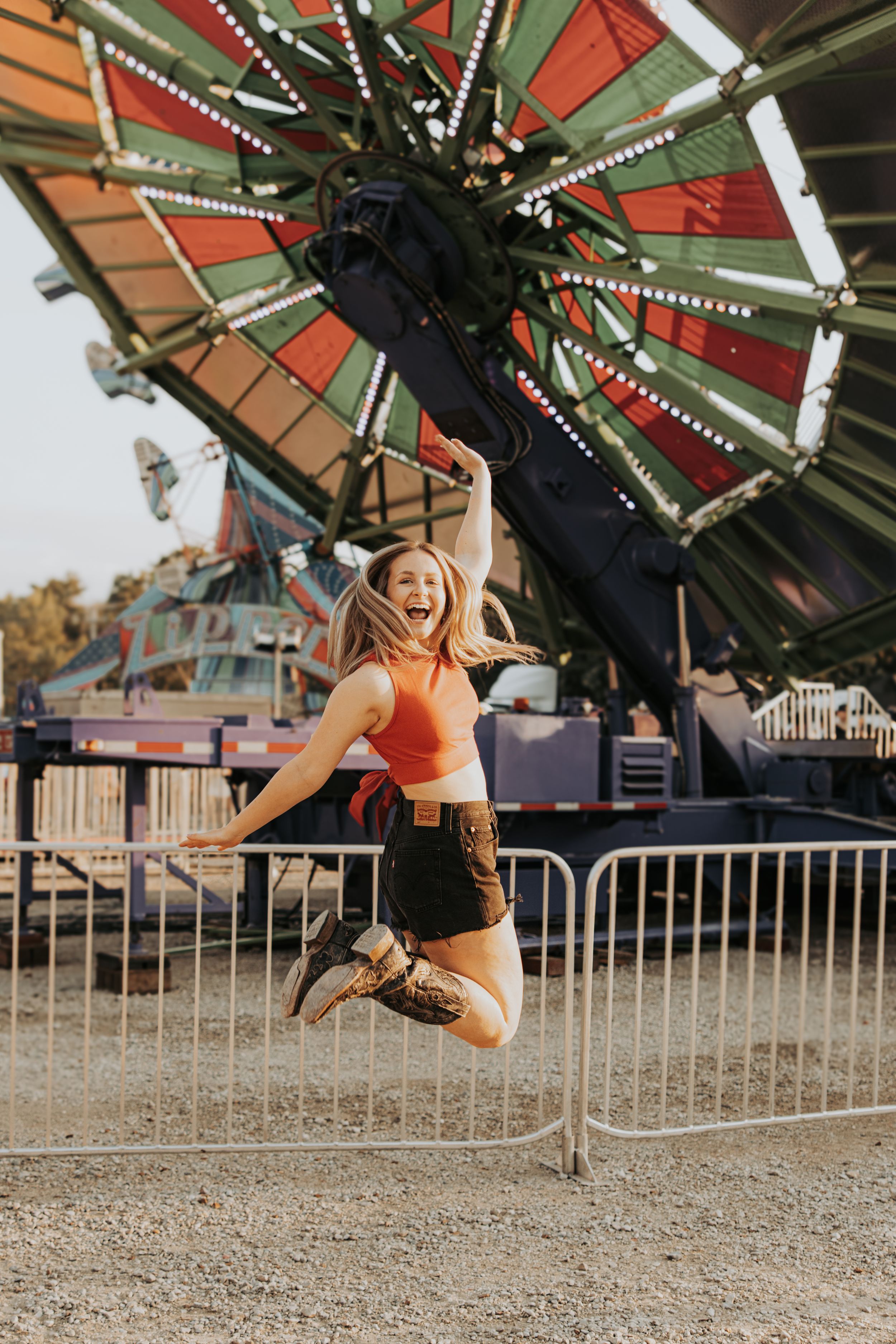 Someone jumping and hanging from carnival ride arms at a fairground with string lights visible overhead.