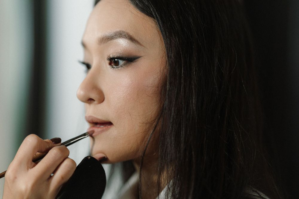 Makeup artist applying lipstick during a beauty session in natural lighting.