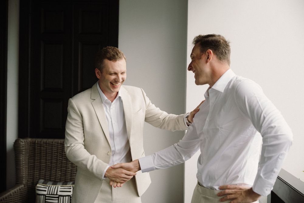 People in white attire laughing and embracing in a bright room.