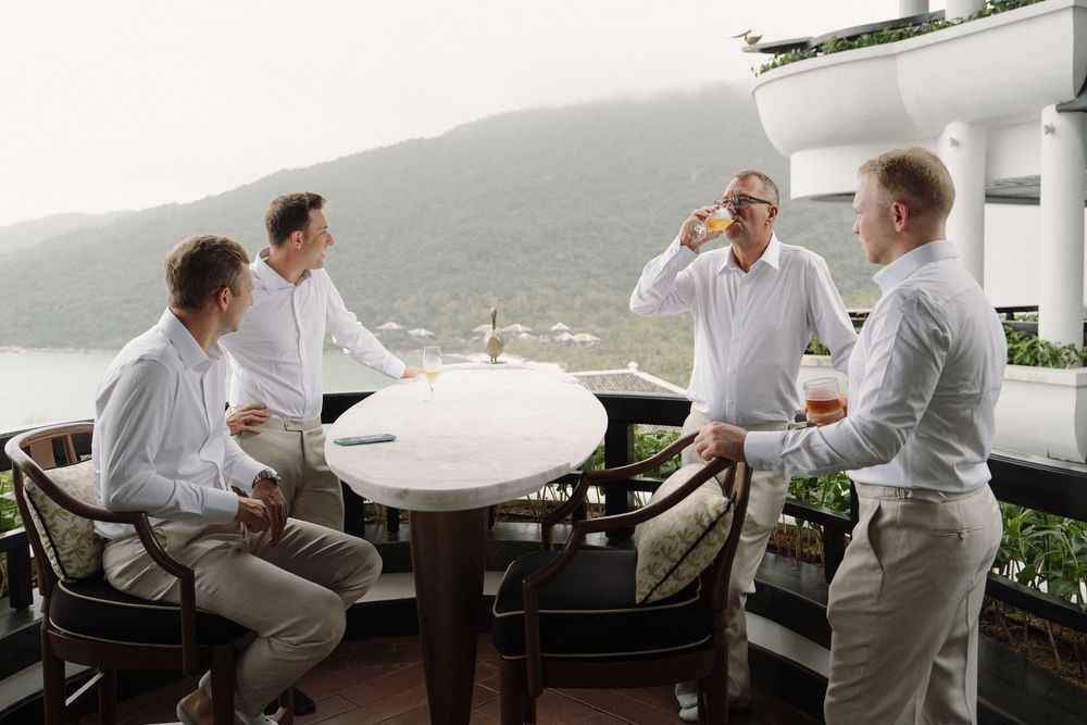 Groomsmen in light colored suits relax on outdoor furniture with a scenic mountain view in the background.