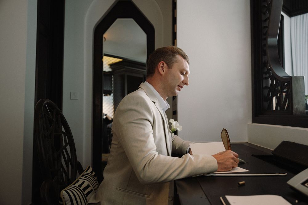 Person in white suit sitting at desk reviewing documents in office setting.