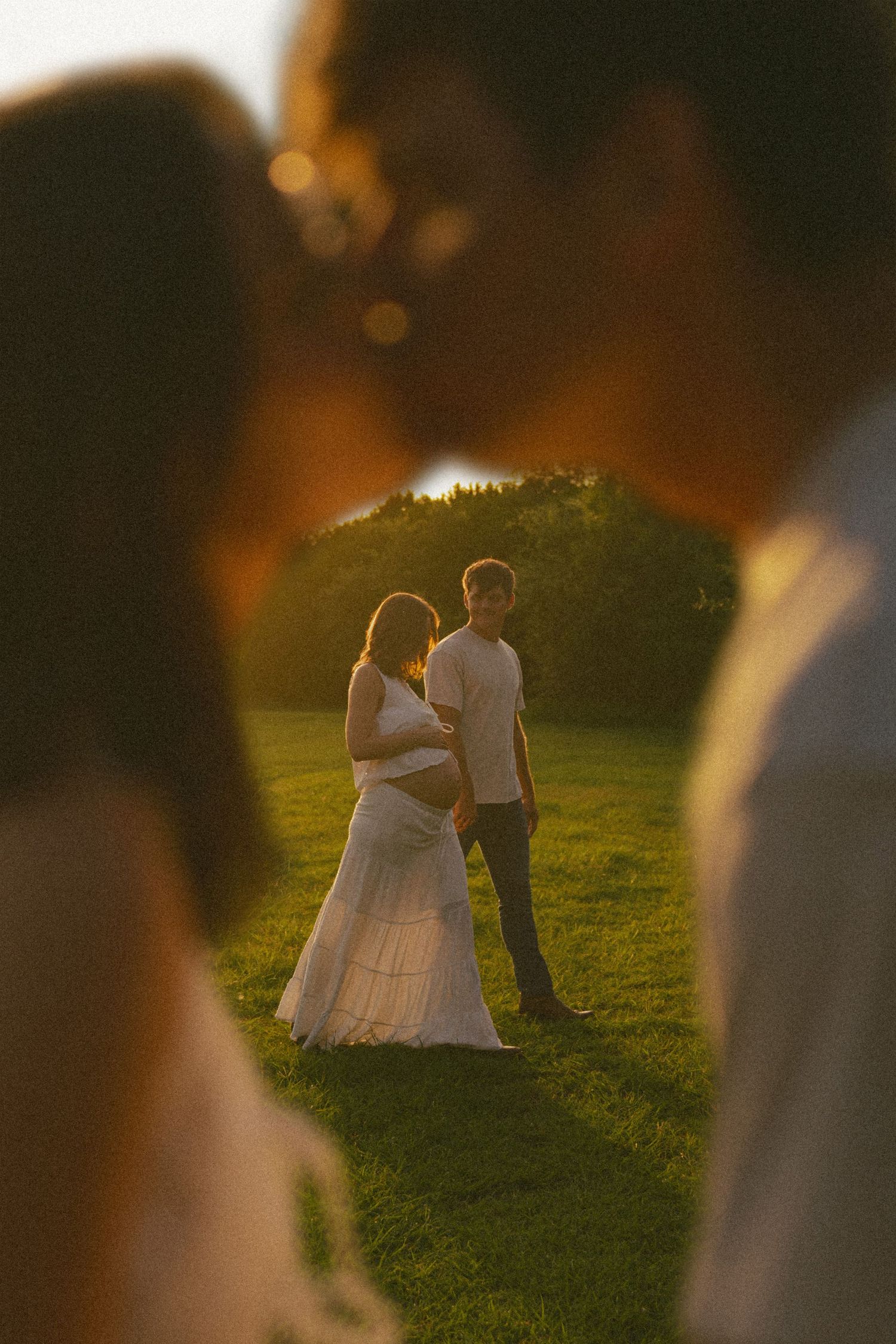Wedding couple photographed through blurred foreground during golden hour in garden setting.