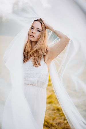 Ethereal bridal portrait with flowing veil against soft natural backdrop.