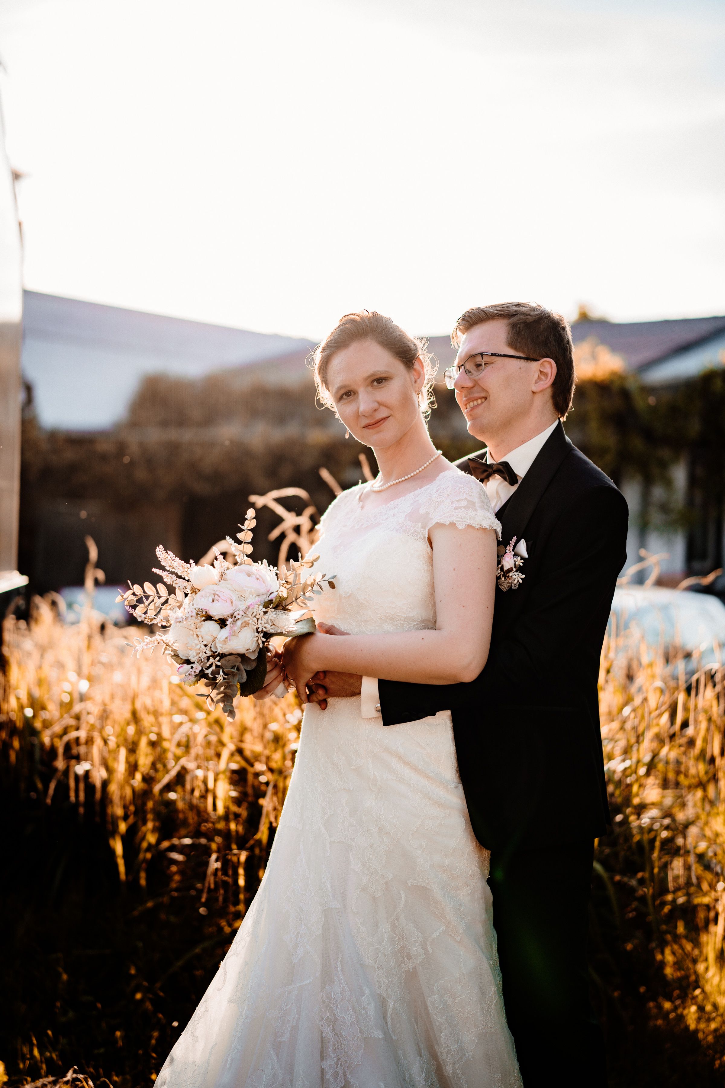 Bride and groom pose together in wheat field during sunset wedding photos.