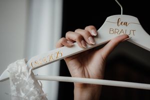 White wooden bridal hanger with gold 'braut' text lettering held against dark background.
