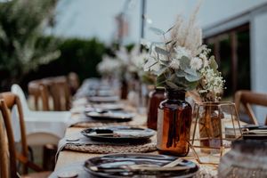 Rustic outdoor wedding table setting with amber bottles and eucalyptus centerpieces.
