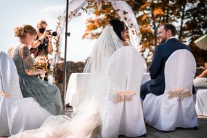 Outdoor wedding ceremony setup with white chairs and floral arch during golden hour.