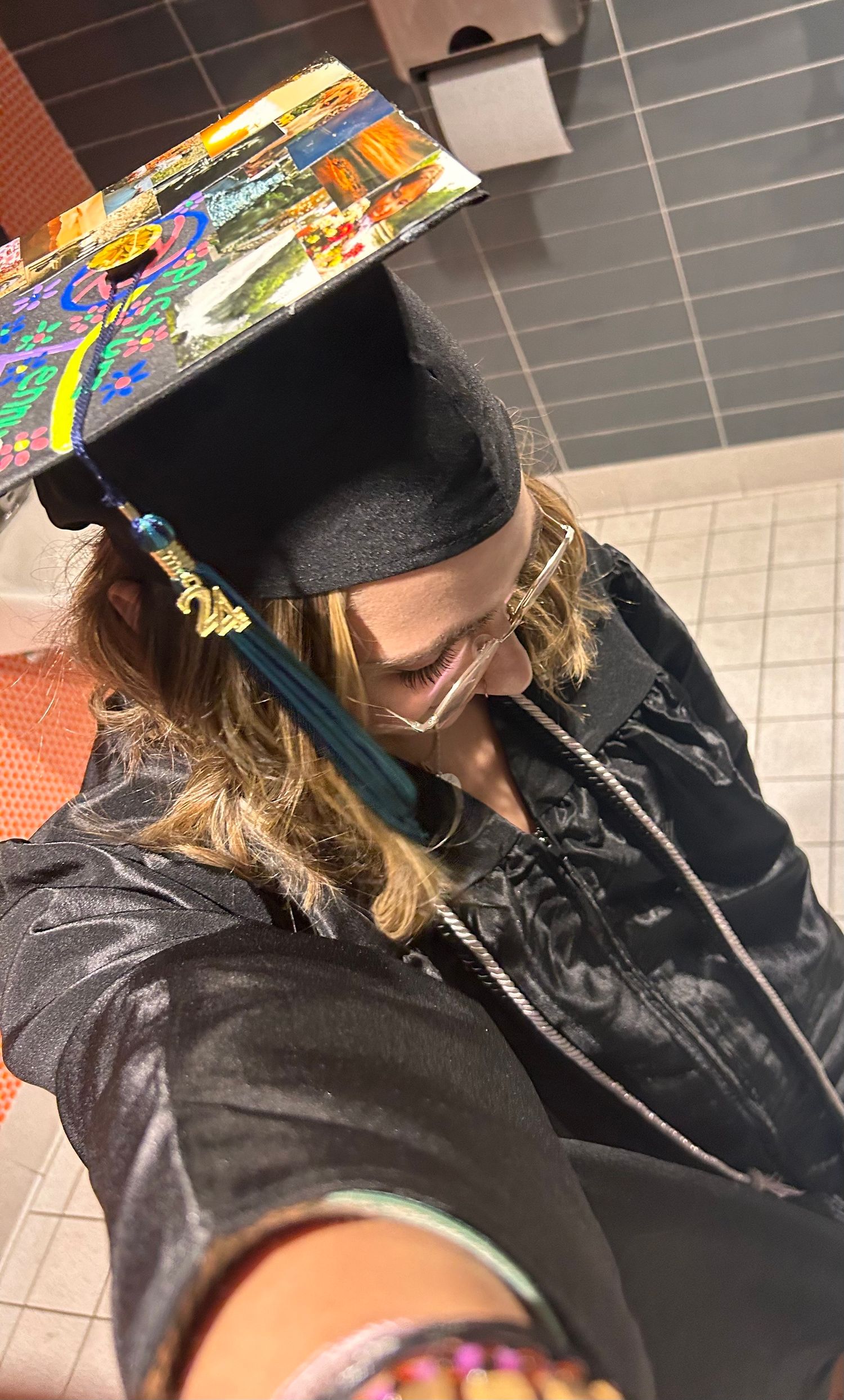 A graduate student looking down while wearing a black cap and gown during commencement ceremony indoors.