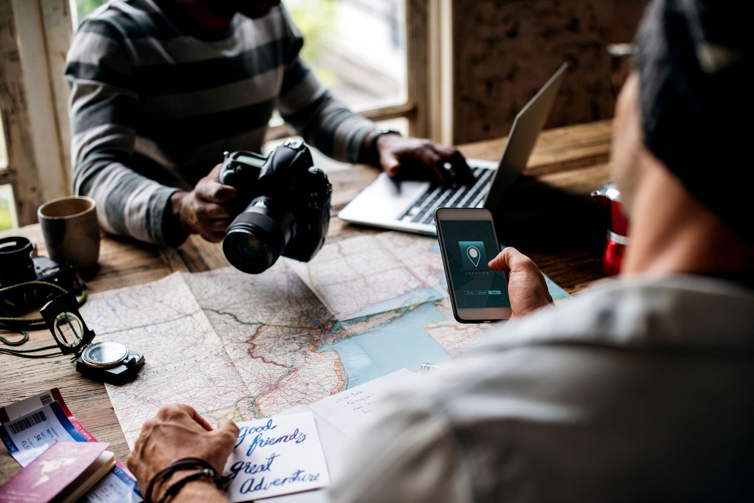 People sitting together at a table with maps and laptops planning an adventure or trip with outdoor gear nearby.