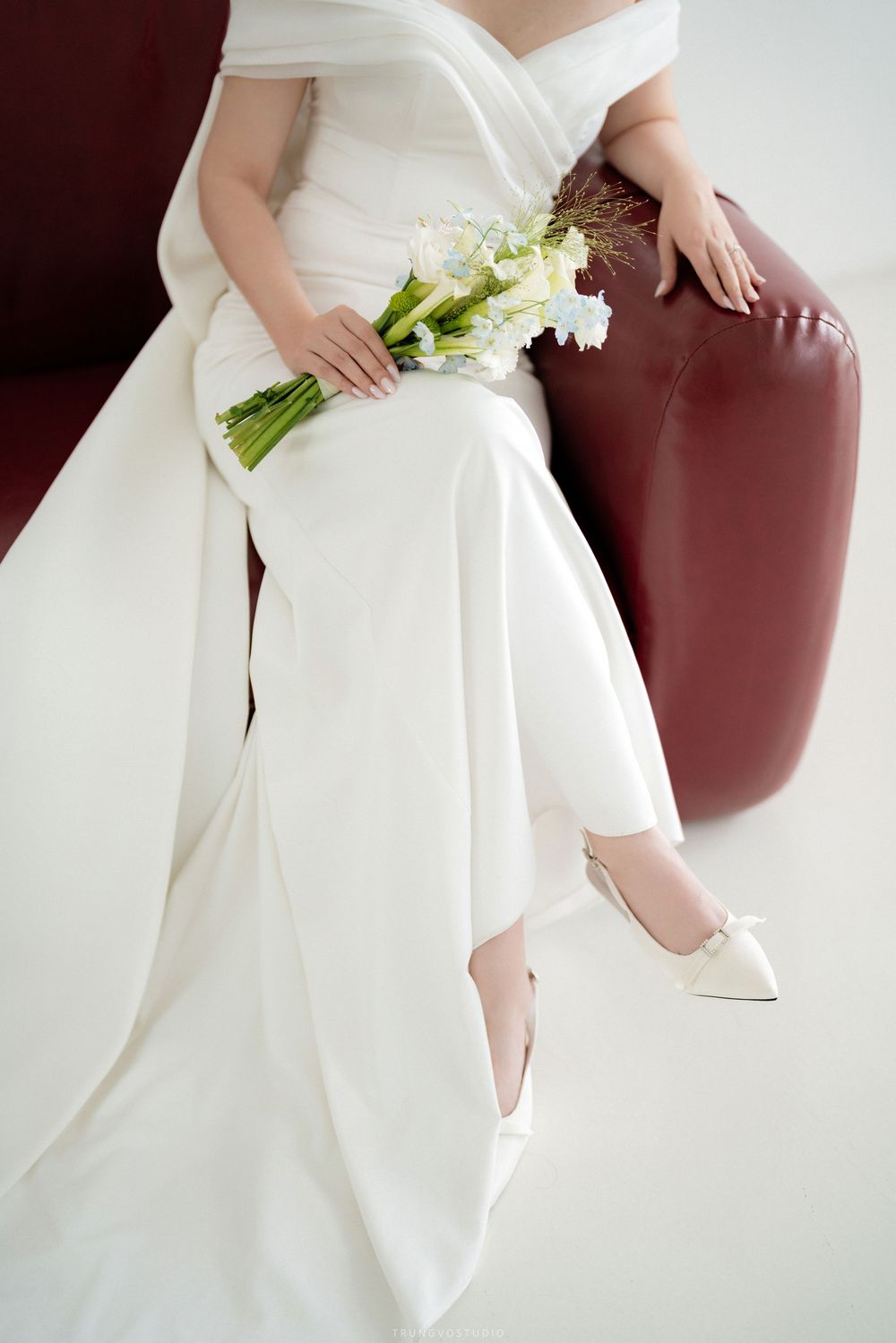 Close-up of bride in white wedding dress holding calla lily bouquet with bridal heels visible.
