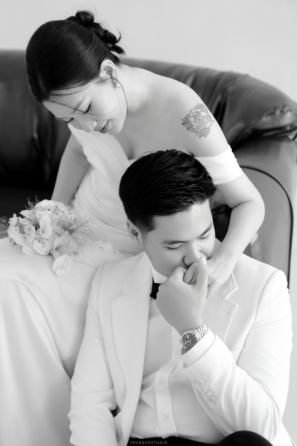 Black and white romantic wedding photo of groom kissing bride's hand while she smiles down at him.