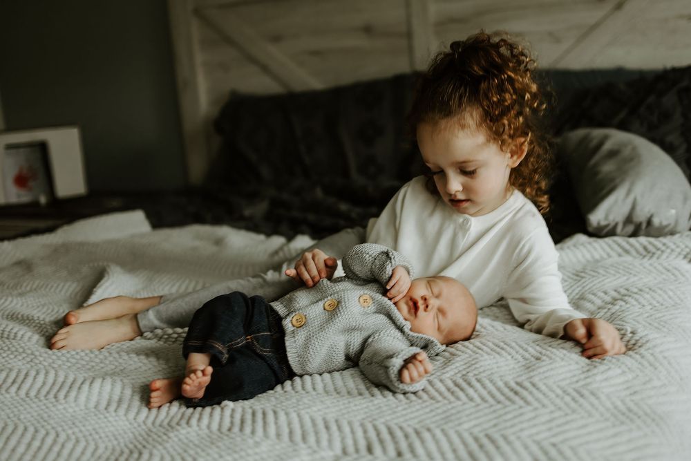 Young child playing with dolls on a white bed.