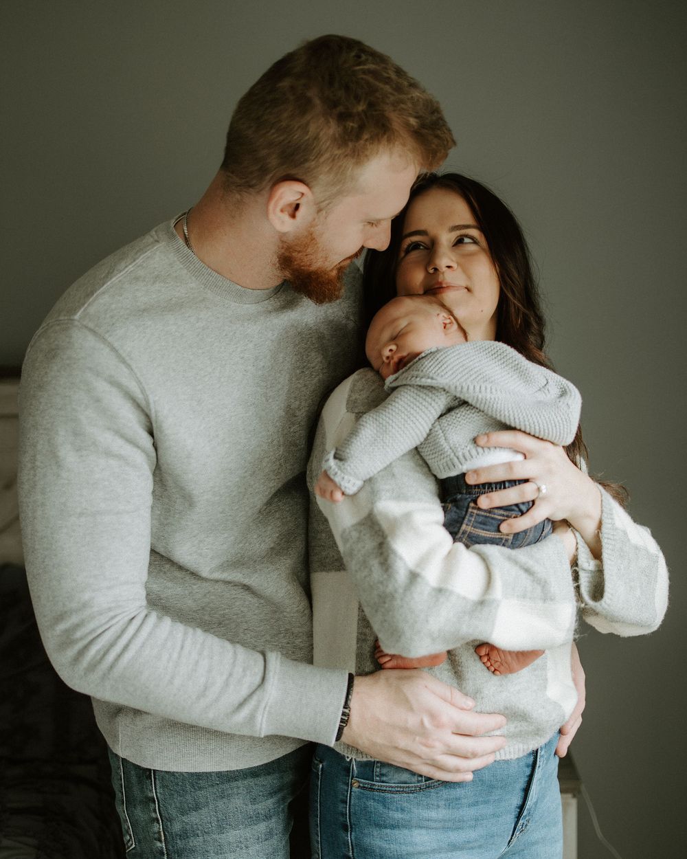 A series of gentle family moments photographed in soft, moody lighting against a grey background.
