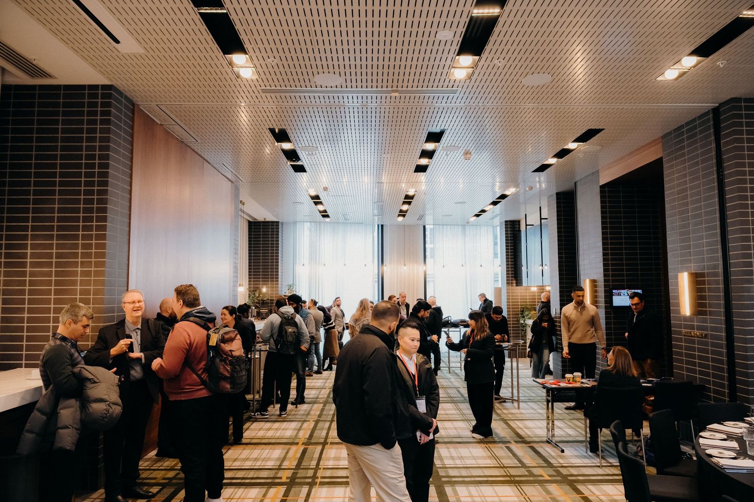 People gather in a modern office hallway with sleek lighting and geometric ceiling details during a business event.